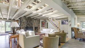 A spacious living room with a stone fireplace, wooden beams, and a large window. - Snowmass Home w/ Hot Tub, Fireplace, & Mtn Views! (Snowmass)