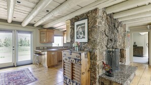 A spacious kitchen with wooden cabinets, a stone accent wall, and a large window offering a view of the outdoors. - Snowmass Home w/ Hot Tub, Fireplace, & Mtn Views! (Snowmass)