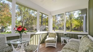 A covered porch with wicker furniture, a glass table, and a view of a residential neighborhood. - Four Generations (Saugatuck)