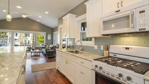 A modern kitchen with white cabinets, a stainless steel sink, a microwave, and a gas stove. - Four Generations (Saugatuck)