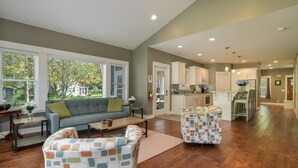 A spacious living room with a sofa and armchairs, a kitchen with white cabinets, and a dining area with a table and chairs. - Four Generations (Saugatuck)