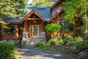 A log cabin with a stone entrance, large windows, and a well-maintained garden. - Northstar Home w/Creekside Views | Shuttle Access (Truckee)