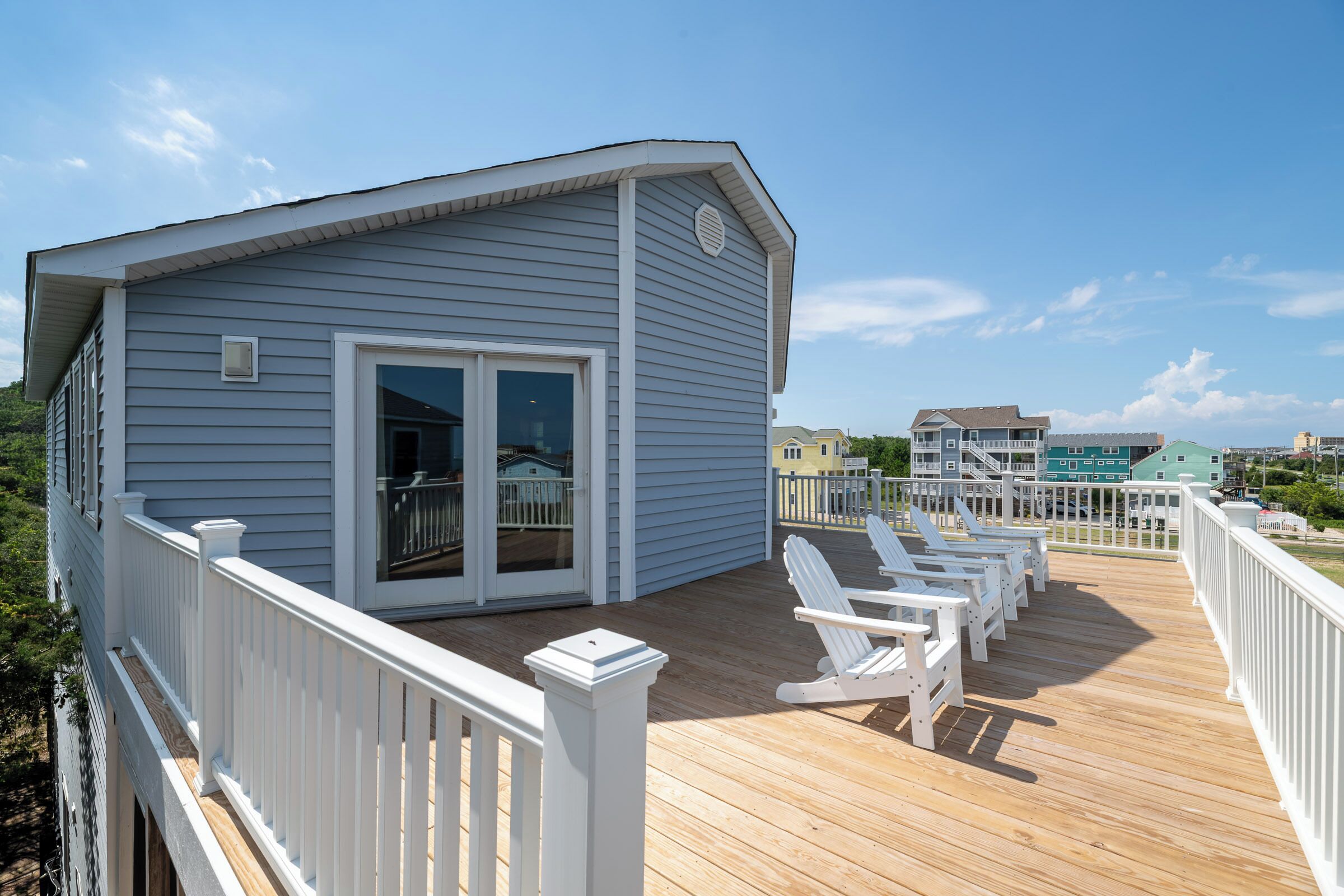 A deck with white railings and chairs, a building with a sliding glass door, and a clear sky.