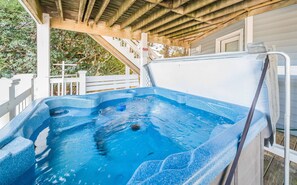 A hot tub under a wooden pergola with a white railing and a staircase in the background.