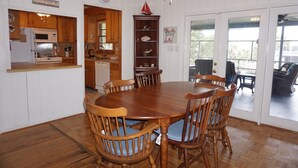 A dining area with a wooden table and chairs, a kitchen with wooden cabinets, a clock, and a sign that reads "Come & coast." - Pryor Dog Friendly, Huge Porch, Creek Dock (Pawleys Island)