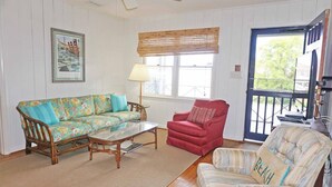 A living room with a sofa, armchair, and ottoman, a glass coffee table, a lamp, and a window with a view. - Pryor Dog Friendly, Huge Porch, Creek Dock (Pawleys Island)