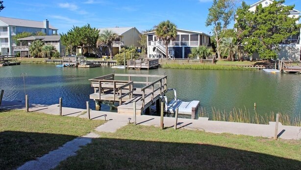 A lakeside property with a dock, a small boat, and a house with a balcony overlooking the water. - Pryor Dog Friendly, Huge Porch, Creek Dock (Pawleys Island)
