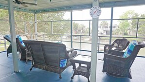 A covered outdoor seating area with wicker furniture and a clock on the wall. - Pryor Dog Friendly, Huge Porch, Creek Dock (Pawleys Island)
