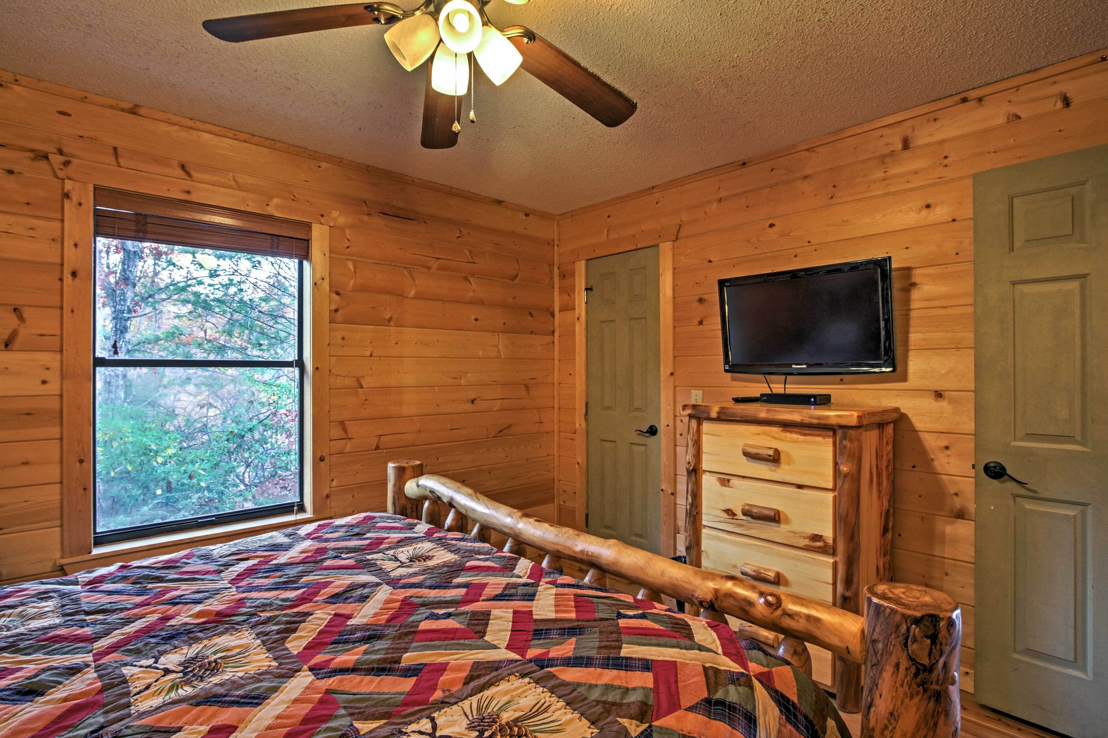 Una habitación de cabaña de madera con una cama, un televisor y una ventana con vistas a árboles.
