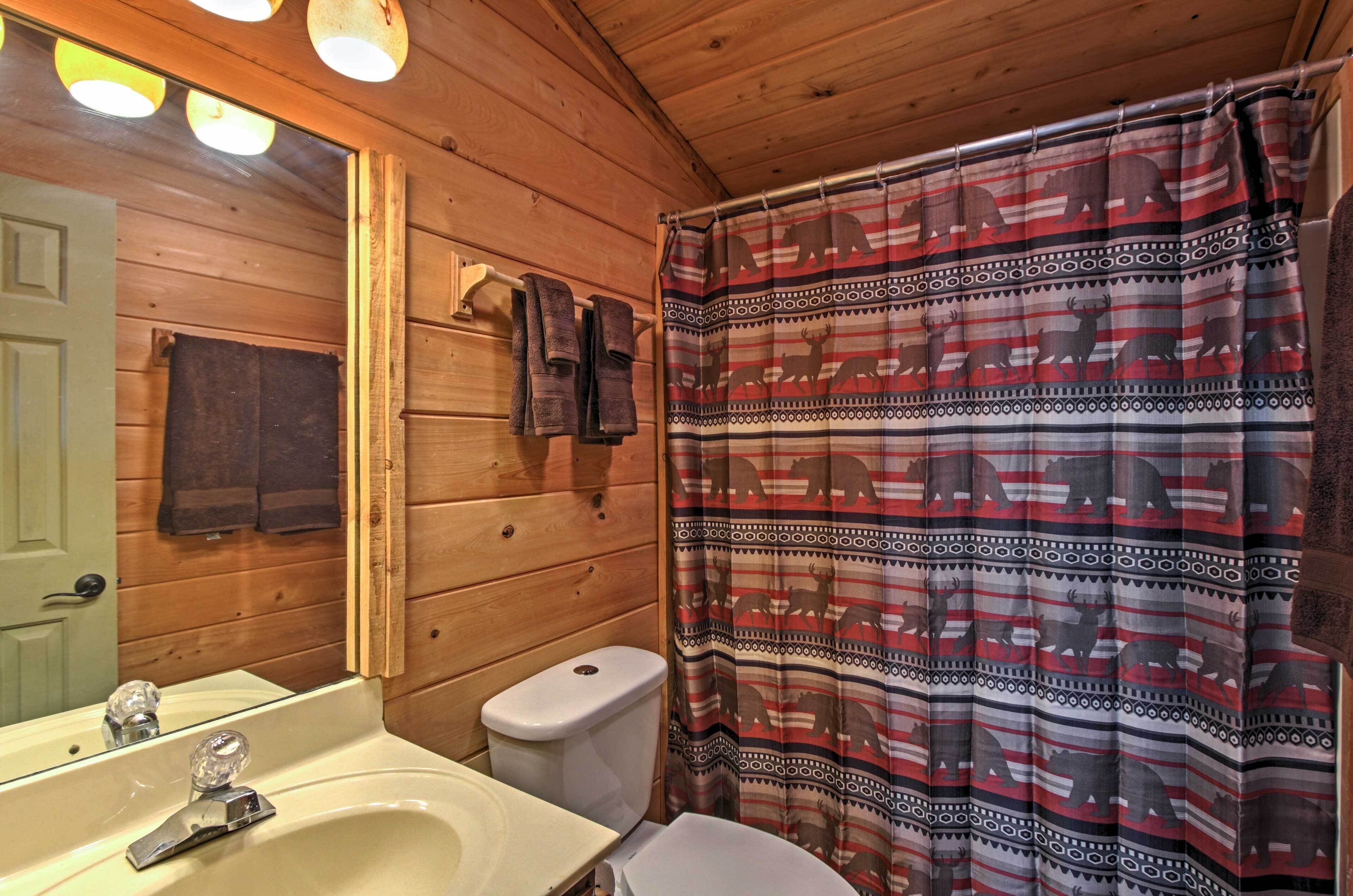 Baño de cabaña de madera con lavamanos, inodoro y cortina de ducha con estampado de animales.