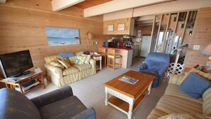Ein gemütliches Wohnzimmer mit einer Couch, einem Couchtisch und einem Fernseher. Es gibt eine Küchenzeile mit einem Kühlschrank und einer Mikrowelle.