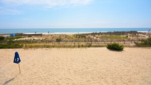 Ein sandiger Strand mit einem blauen Sonnenschirm und einem Zaun im Hintergrund.