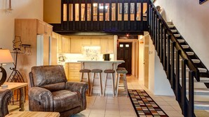 A spacious living area with a leather armchair, a wooden coffee table, and a kitchen with a bar area. - Stunning Views! Walk to Lifts/Downtown! (Breckenridge)