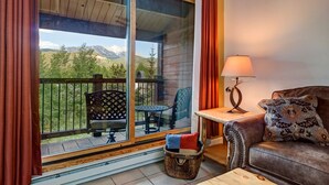 A cozy room with a balcony, a sofa, a table, and a lamp. - Stunning Views! Walk to Lifts/Downtown! (Breckenridge)