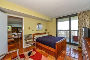 Et hotelværelse med seng, stol, skrivebord med fjernsyn, balkon med udsigt og spiseplads med stole og bord.