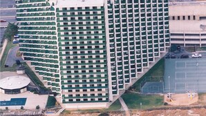 A high-rise hotel with a unique triangular shape, multiple floors, and a parking lot in the foreground. - Charming, unique 2-bedroom oceanfront condo with southwest decor, free WiFi, an indoor and outdoor pool, and more located uptown just steps from the beach! (Ocean City)