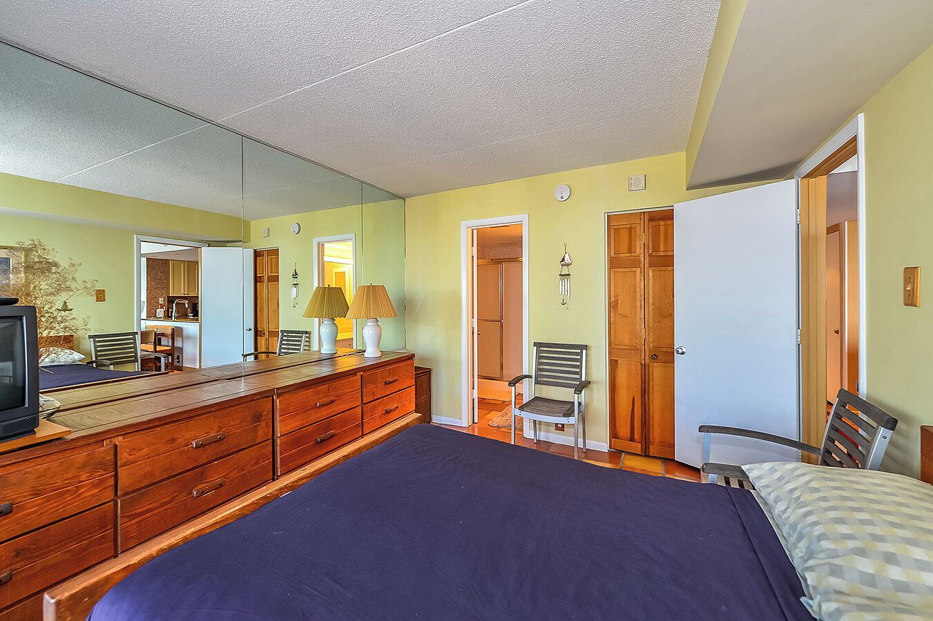 A bedroom with a large bed, wooden dresser, two lamps, a chair, and a mirror.