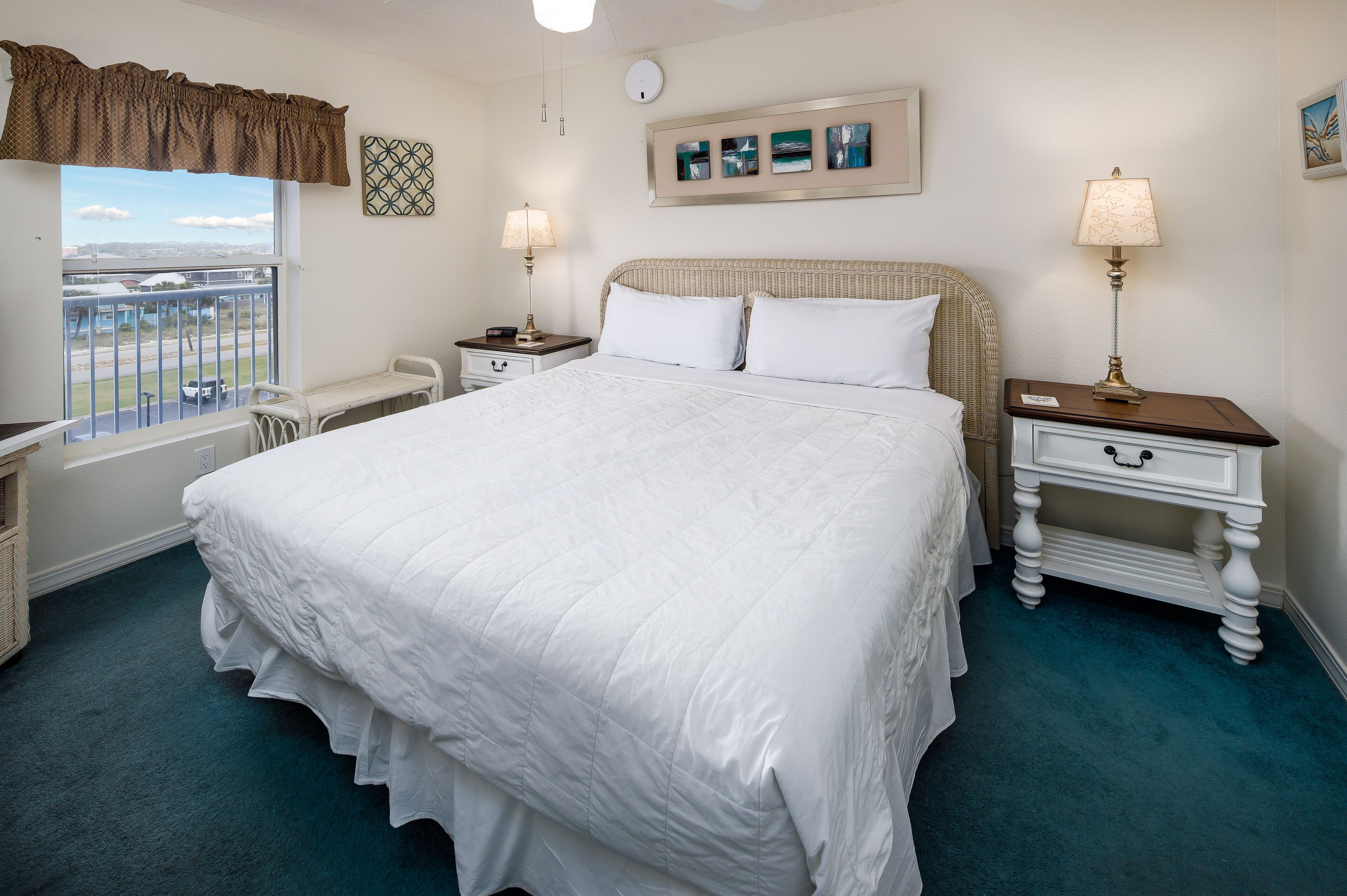 A neatly arranged hotel room with a large bed, two bedside tables with lamps, a view through a window, and a wall with framed pictures.
