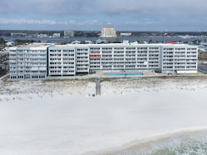 A beachfront hotel with multiple balconies, a swimming pool, and a view of the ocean and city skyline.