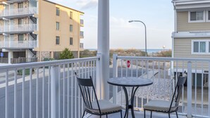 A balcony with two chairs and a table, overlooking a street with buildings and a stop sign. - Unique 5BR, 4.5 bath single floor condominium with great ocean views. (Ocean City)