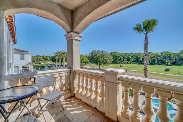 A balcony with a view of a golf course, a palm tree, and a pool.
