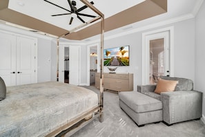 A bedroom with a bed, a grey sofa, a TV, and a ceiling fan. - Showcase Villa | 5BR, 4 Bath Luxe Modern Home w/ Private Pool, Theater, and Game Loft Near Disney (Reunion)