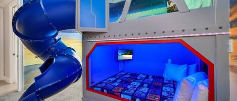 A child's playroom with a slide, a bed with a view, and a TV.