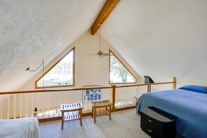 Cozy loft-style room with a bed, wooden bench, and table, offering a view of the outdoors through large windows.