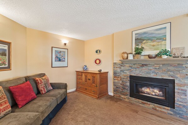 A living room with a fireplace, a sofa, a wooden cabinet, and wall decorations. - Beautiful Breckenridge views, Close to lifts/downtown, Garage parking! (Breckenridge)