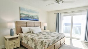 A bedroom with a bed, two bedside tables with lamps, a painting above the bed, and a balcony with a view.