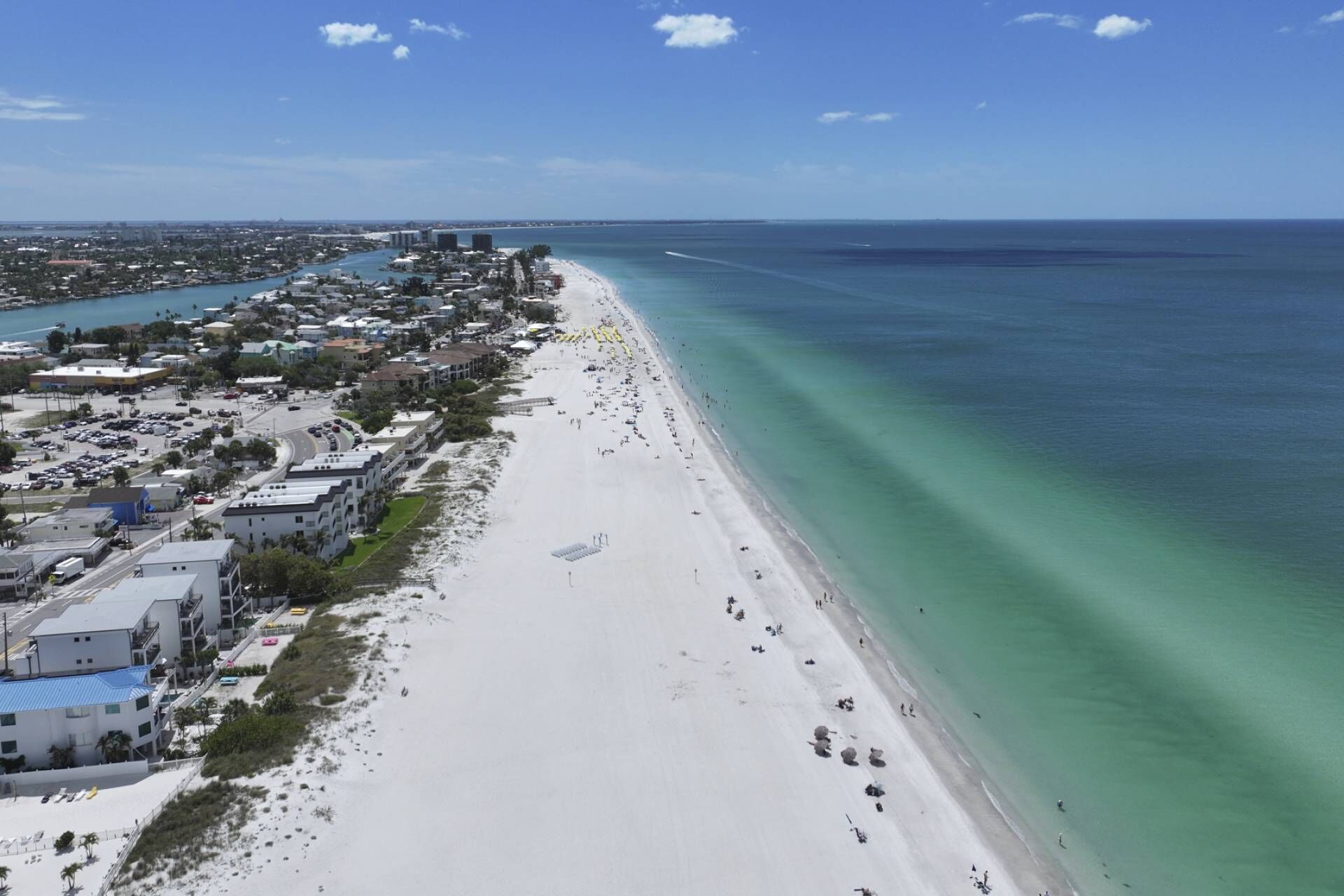 A coastal cityscape with a wide beach, clear blue waters, and a dense urban area with buildings and roads.