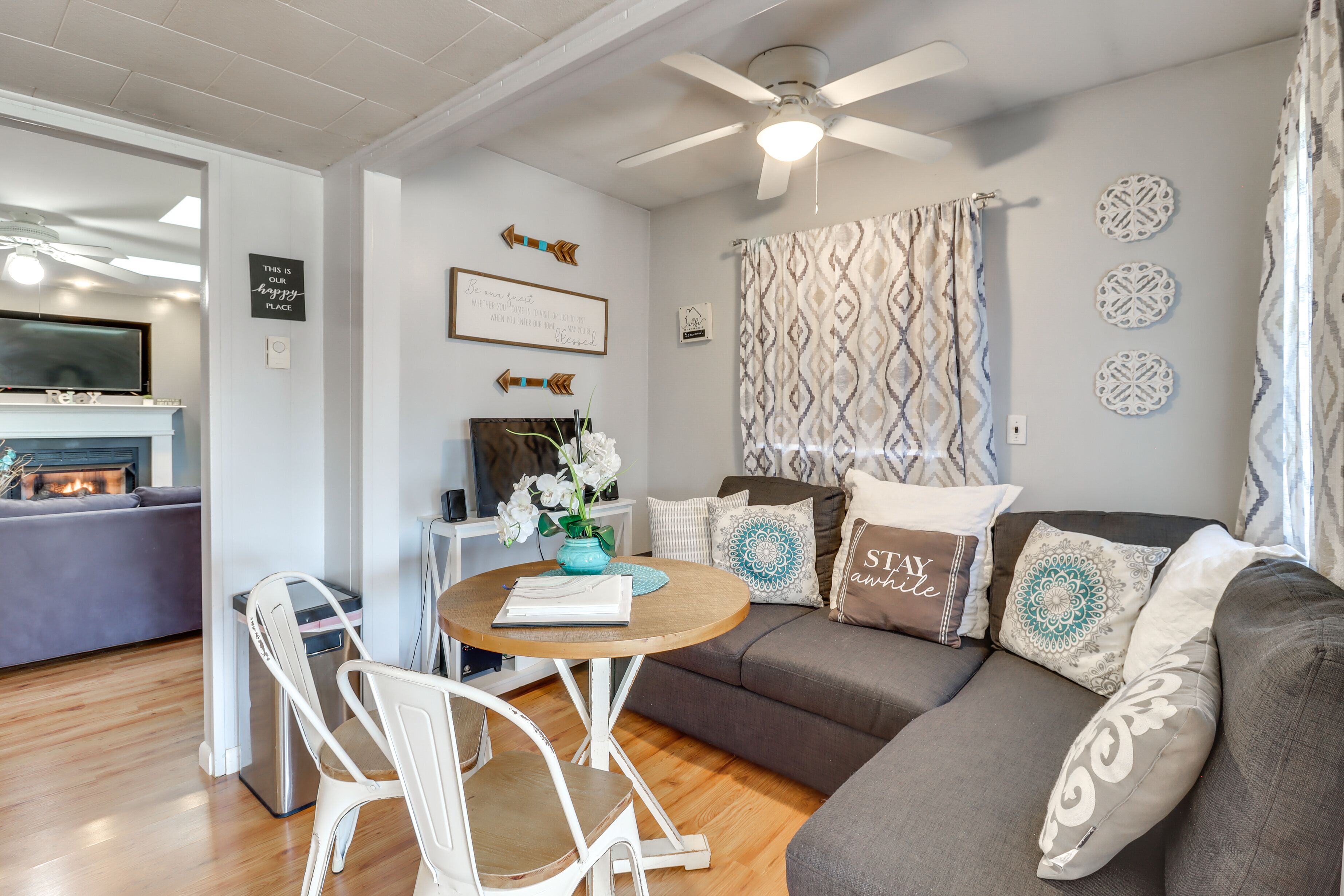 A cozy living room with a gray sofa, white chairs, a wooden coffee table, and a ceiling fan.