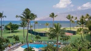 A resort with a pool, palm trees, a golf course, and a view of the ocean.