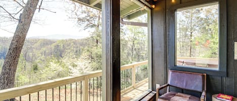 Une terrasse en bois avec un banc et une grande fenĂȘtre donnant sur une zone boisĂ©e.