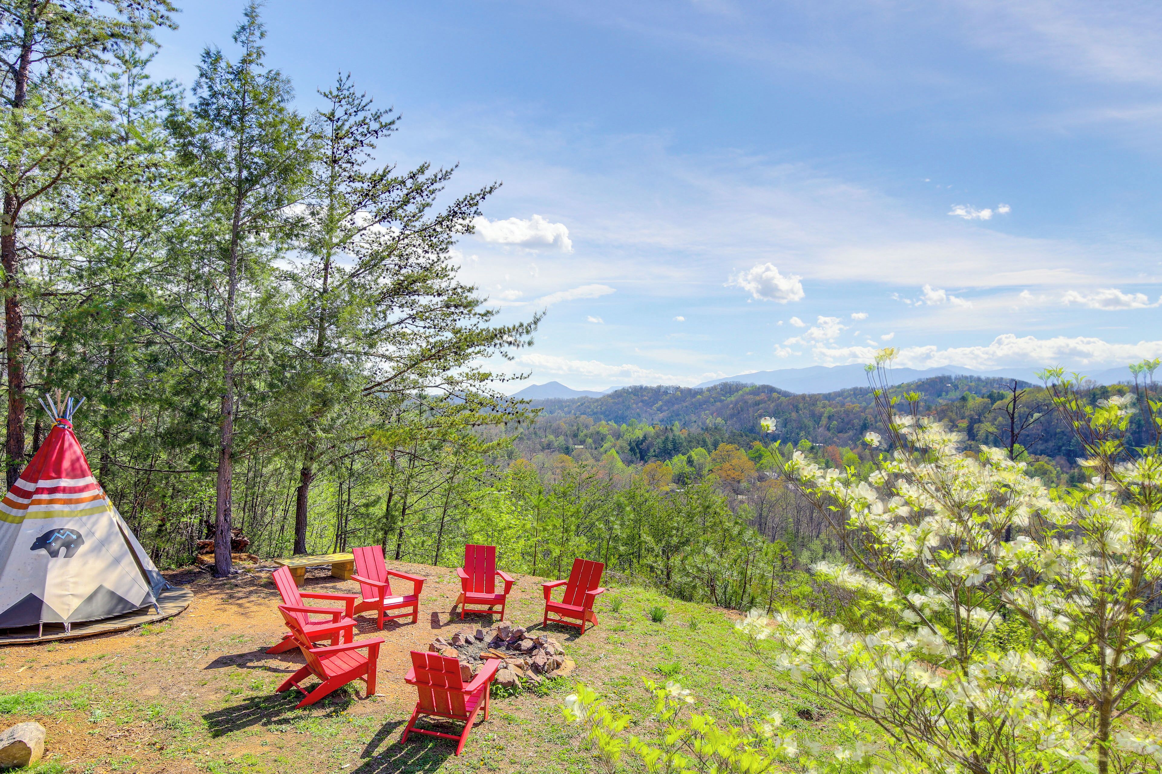 A tent with red chairs and a fire pit in a forested area with a view of mountains.