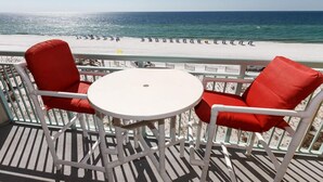 A balcony with white metal chairs and a small white table, overlooking a beach with umbrellas. - PI 406: Sunset Shores - Take A Look! Perfect Beach Retreat with Beach Service (Fort Walton Beach)