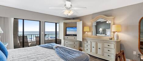 Habitación de hotel con cama, televisor, cómoda, espejo y balcón con vista al océano.