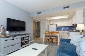 Ein gemütlicher Wohnraum mit Fernseher, Bücherregal, Essbereich, Küche und einer Couch.