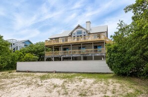 A multi-story beachfront house with a wooden deck and a covered porch.