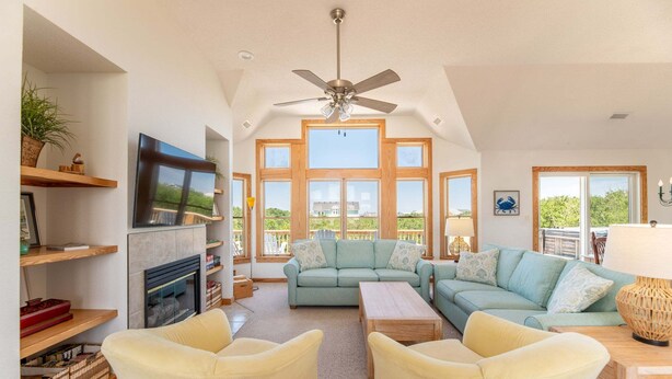 A spacious living room with a fireplace, a ceiling fan, and large windows. - Rookery - Corolla, Whalehead, 395 Yds to Beach, Ocean View, Pool, Hot Tub, Pets OK, Flex Stays (Corolla)