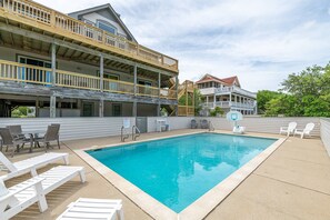 Une piscine avec des chaises longues, un panier de basketball et une terrasse en bois dotée de rampes.