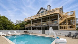 A pool with lounge chairs, a wooden deck, and a two-story building with a balcony. - Rookery - Corolla, Whalehead, 395 Yds to Beach, Ocean View, Pool, Hot Tub, Pets OK, Flex Stays (Corolla)