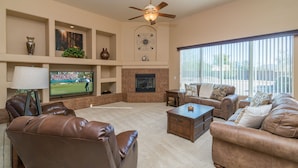 A spacious living room with a fireplace, leather sofas, a television, and a large window.