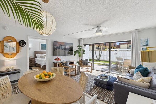 A modern living room with a dining area, a ceiling fan, and a view of the backyard through glass doors.