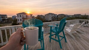 A wooden deck with turquoise chairs and a white mug, overlooking a residential area during sunset. - Time to Paws & Reflect - Corolla, Ocean Sands, Ocean View, Beach 260 Yds, Pool, Pets OK, Flex Stays (Corolla)