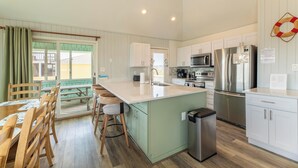 A modern kitchen with a central island, stainless steel appliances, and a view to the outside. - Time to Paws & Reflect - Corolla, Ocean Sands, Ocean View, Beach 260 Yds, Pool, Pets OK, Flex Stays (Corolla)
