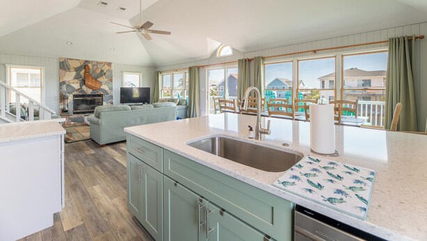 A spacious kitchen with a large island, a dining area with outdoor seating, and a view of a pool and houses. - Time to Paws & Reflect - Corolla, Ocean Sands, Ocean View, Beach 260 Yds, Pool, Pets OK, Flex Stays (Corolla)