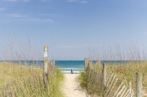 A beach path leading to the ocean with a wooden fence and a signpost.