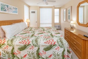 Une chambre à coucher avec un lit, une commode, un miroir et un ventilateur de plafond.