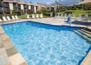 Une piscine à l’eau d’un bleu cristallin, entourée de chaises longues et bordée d’une terrasse carrelée.